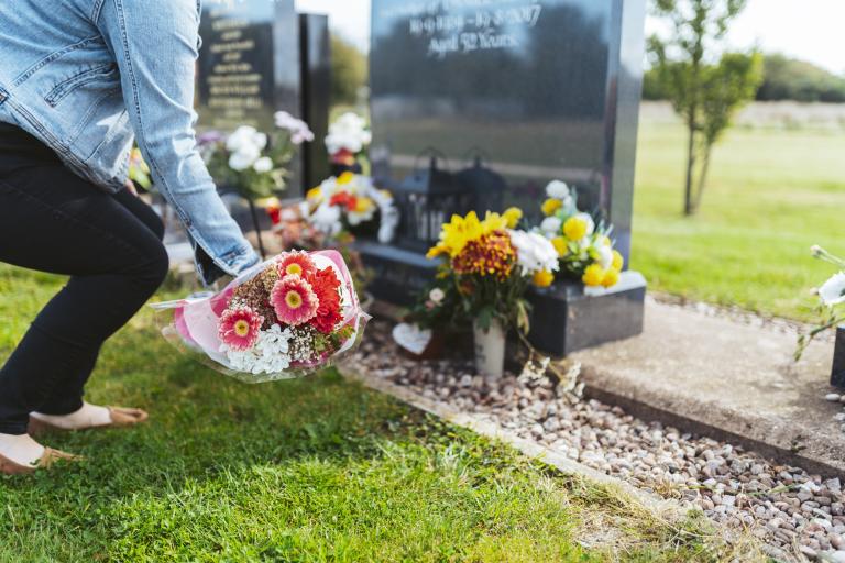 A woman lays a bouquet at a grave in Strawberry Lane Cemetery, Great Wyrley